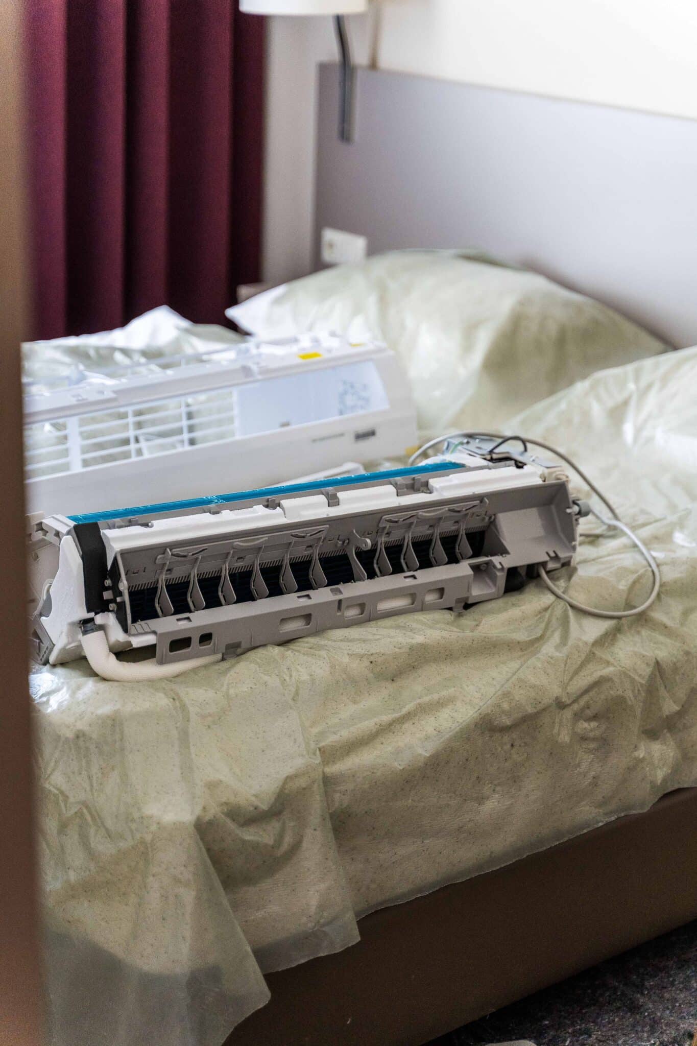 Ein auseinandergebautes Klimaanlagen-Innengerät liegt auf einem Bett, das mit Folie abgedeckt ist.