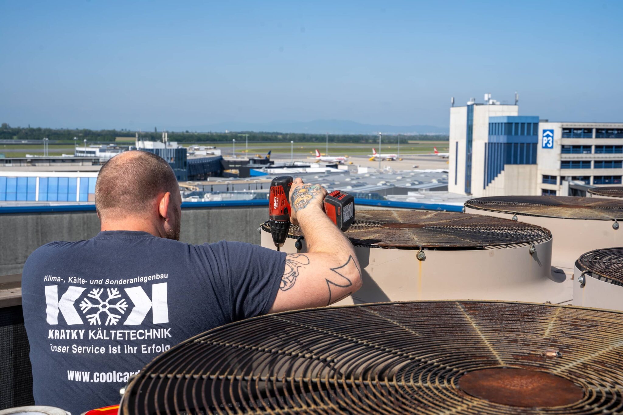 Kältetechniker wartet Industriekühlanlage mit Akkuschrauber auf dem Dach eines Flughafens in Wien